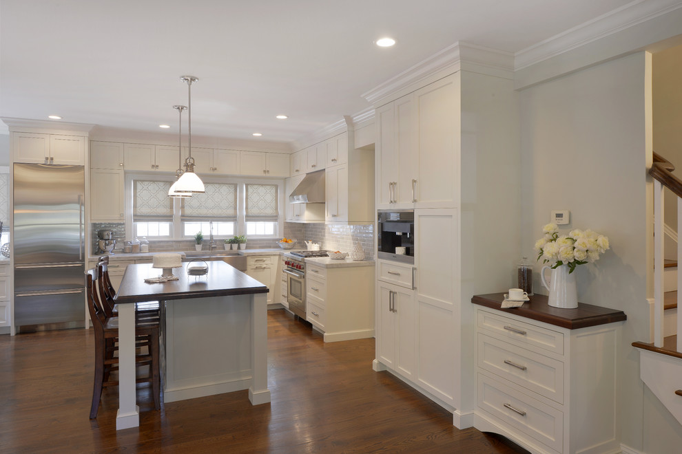 This is an example of an expansive transitional l-shaped eat-in kitchen in New York with a farmhouse sink, shaker cabinets, white cabinets, marble benchtops, grey splashback, ceramic splashback, stainless steel appliances, dark hardwood floors and with island.