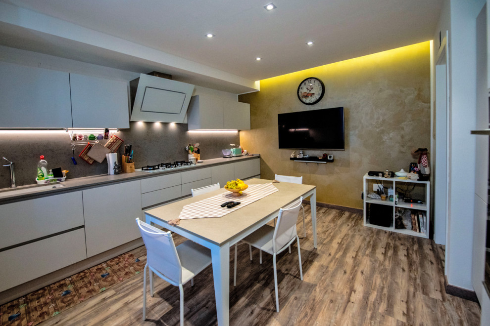 Mid-sized contemporary single-wall open plan kitchen in Other with an undermount sink, beaded inset cabinets, white cabinets, quartz benchtops, beige splashback, porcelain splashback, white appliances, porcelain floors, no island, brown floor and beige benchtop.