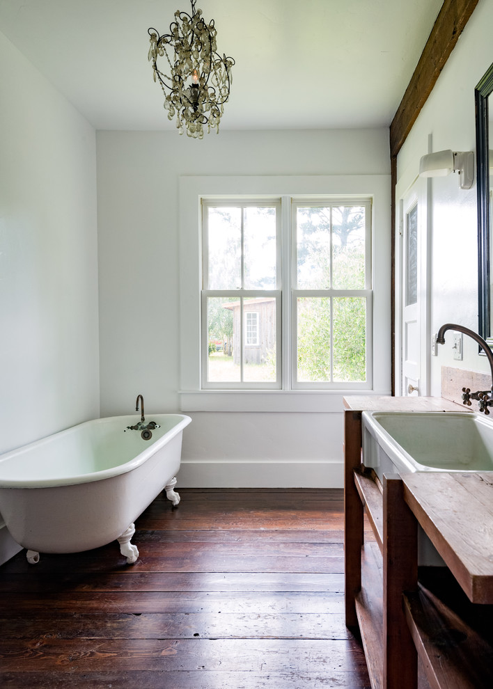 This is an example of a country bathroom in San Francisco with open cabinets, medium wood cabinets, a claw-foot tub, white walls, dark hardwood floors, wood benchtops, brown floor and brown benchtops.