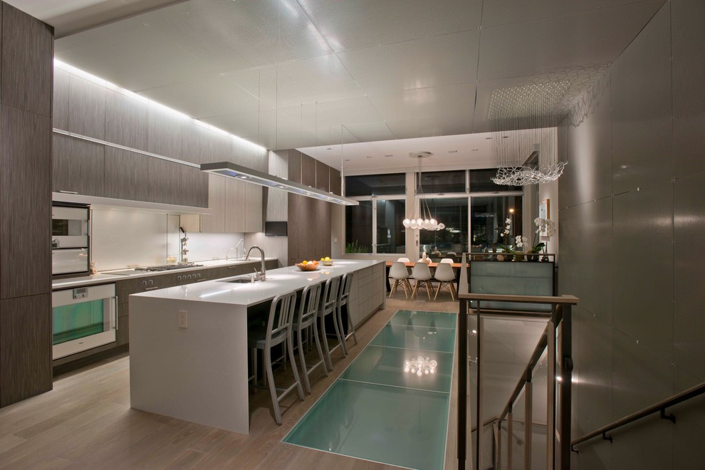 This is an example of a contemporary galley eat-in kitchen in San Francisco with an undermount sink, flat-panel cabinets, grey cabinets, white splashback, white appliances, light hardwood floors and with island.