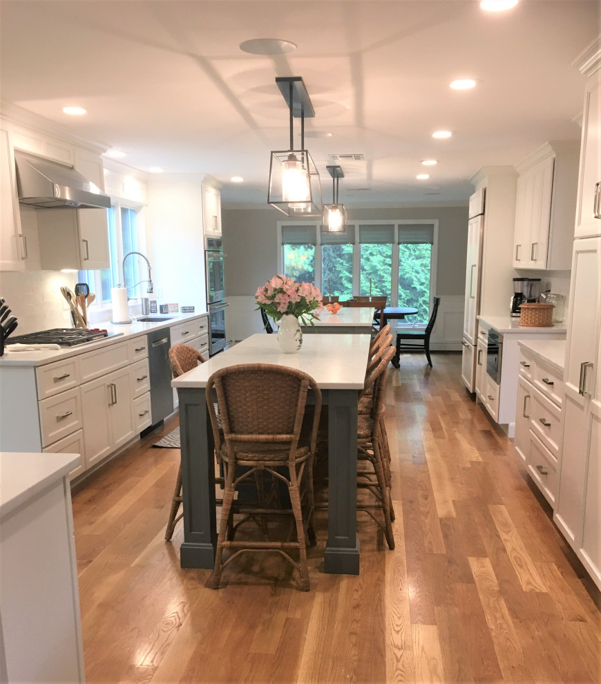 Example of a large transitional galley light wood floor and brown floor eat-in kitchen design in Boston with an undermount sink, shaker cabinets, white cabinets, quartz countertops, white backsplash, subway tile backsplash, stainless steel appliances, two islands and white countertops