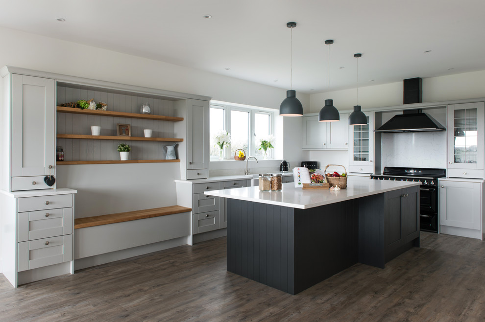 Design ideas for a large transitional l-shaped eat-in kitchen in Devon with a farmhouse sink, shaker cabinets, grey cabinets, quartzite benchtops, white splashback, glass sheet splashback, black appliances, laminate floors, with island, white benchtop and brown floor.