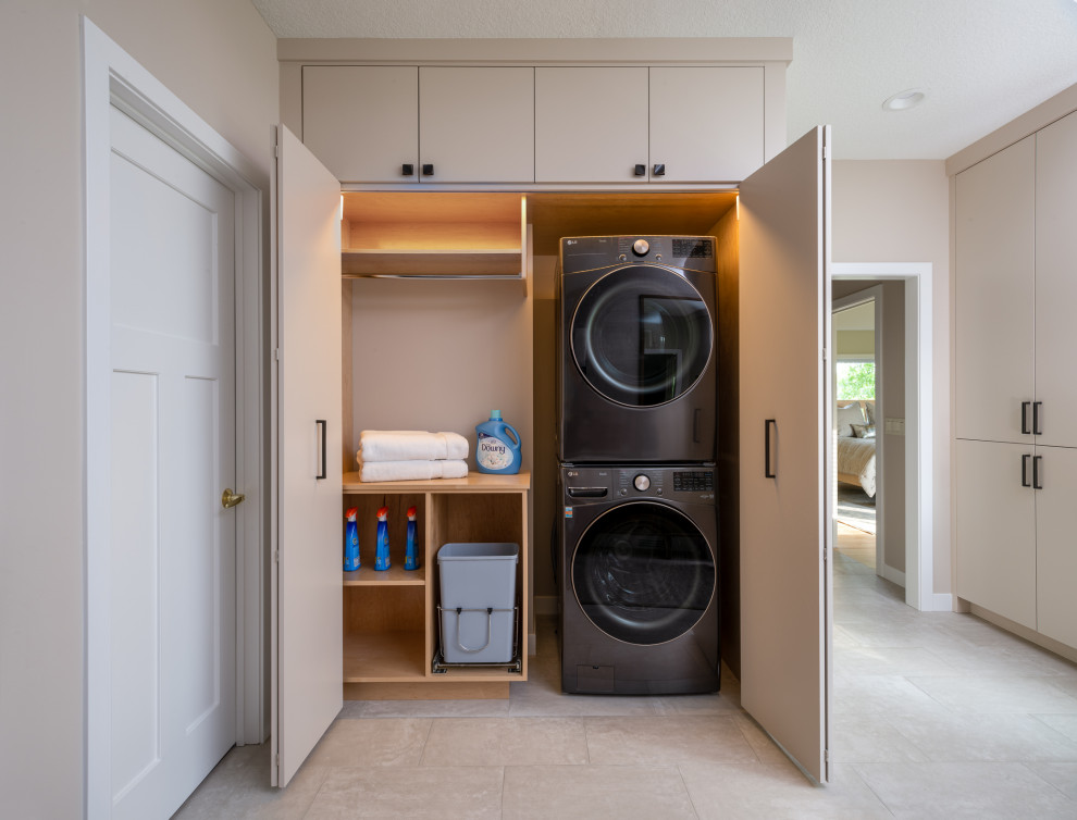 Inspiration for a mid-sized contemporary single-wall laundry cupboard in Minneapolis with flat-panel cabinets, a concealed washer and dryer, beige cabinets, grey walls, ceramic floors and white floor.