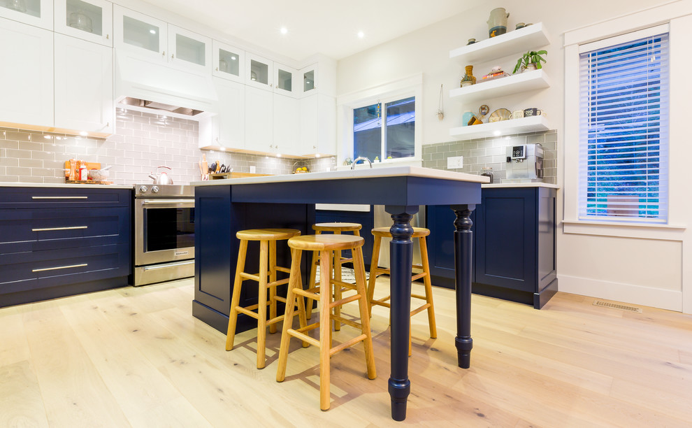 Example of a large transitional u-shaped light wood floor open concept kitchen design with a farmhouse sink, shaker cabinets, blue cabinets, quartz countertops, gray backsplash, glass tile backsplash, stainless steel appliances, an island and white countertops