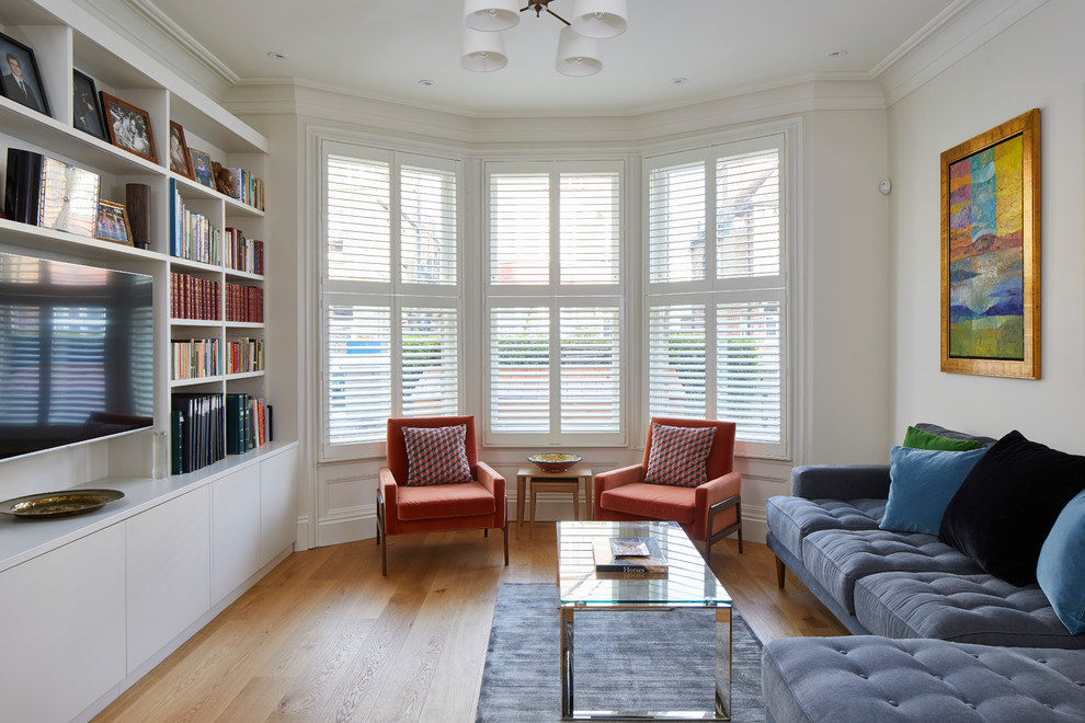 This is an example of a transitional living room in London with white walls, medium hardwood floors, a wall-mounted tv and brown floor.