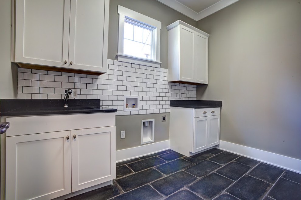 Design ideas for a large traditional single-wall dedicated laundry room in Other with an undermount sink, shaker cabinets, white cabinets, solid surface benchtops, concrete floors, a side-by-side washer and dryer, black floor and grey walls.