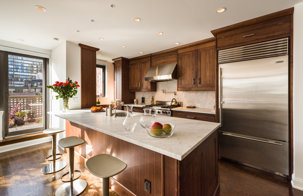 Mid-sized transitional l-shaped kitchen in New York with an undermount sink, shaker cabinets, dark wood cabinets, marble benchtops, white splashback, stone tile splashback, stainless steel appliances, medium hardwood floors, with island and brown floor.