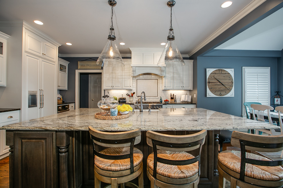 Inspiration for a large transitional l-shaped medium tone wood floor and brown floor open concept kitchen remodel in Charlotte with white cabinets, granite countertops, white backsplash, stainless steel appliances, an island, a farmhouse sink, raised-panel cabinets, porcelain backsplash and white countertops
