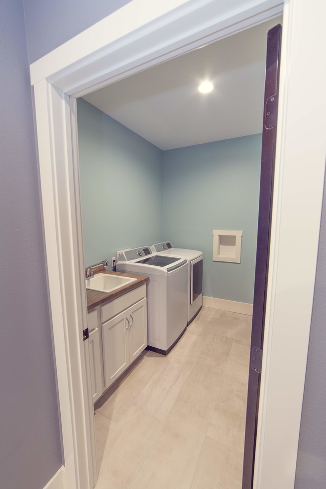 This is an example of a country single-wall dedicated laundry room in Cedar Rapids with an utility sink, recessed-panel cabinets, white cabinets, green walls, porcelain floors, a side-by-side washer and dryer and beige floor.
