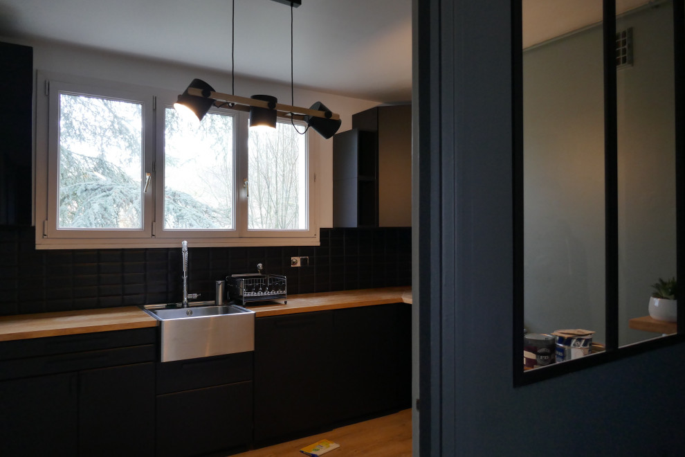 Inspiration for a mid-sized modern u-shaped separate kitchen in Paris with a drop-in sink, flat-panel cabinets, black cabinets, wood benchtops, black splashback, subway tile splashback, stainless steel appliances, vinyl floors, brown floor and brown benchtop.