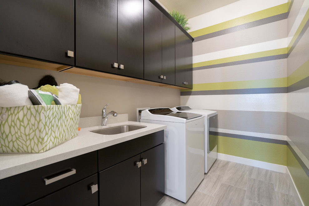 Photo of a mid-sized contemporary single-wall dedicated laundry room in Phoenix with an undermount sink, flat-panel cabinets, black cabinets, marble benchtops, multi-coloured walls, ceramic floors, a side-by-side washer and dryer, grey floor and white benchtop.