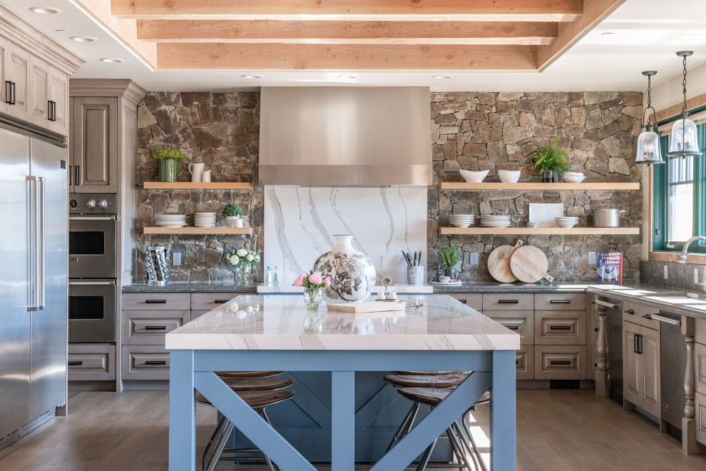 This is an example of a large country u-shaped kitchen in Other with stainless steel appliances, light hardwood floors, with island, raised-panel cabinets, blue splashback, grey benchtop, exposed beam and grey cabinets.