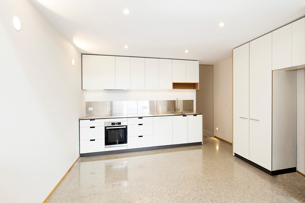Design ideas for a small contemporary single-wall separate kitchen in Melbourne with an integrated sink, flat-panel cabinets, white cabinets, stainless steel benchtops, metallic splashback, stainless steel appliances, concrete floors and no island.