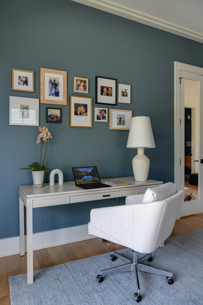 Großes Modernes Arbeitszimmer mit Arbeitsplatz, blauer Wandfarbe, hellem Holzboden, Kamin, Kaminumrandung aus Stein und freistehendem Schreibtisch in Washington, D.C.
