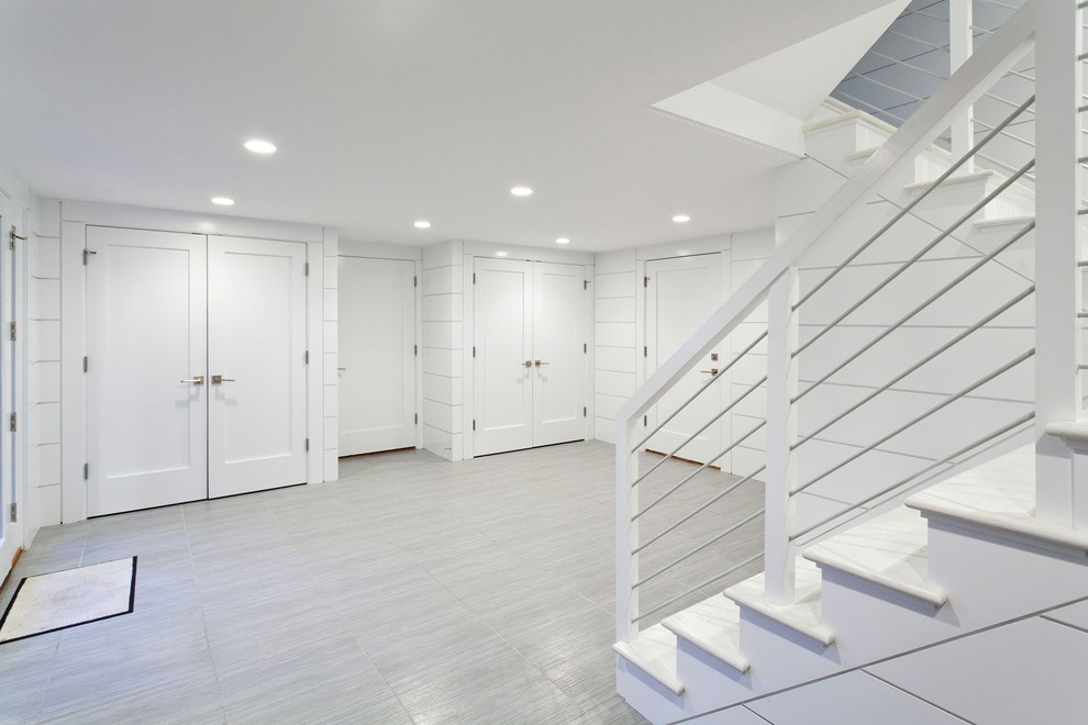 Design ideas for a mid-sized beach style walk-out basement in Boston with white walls, grey floor, slate floors and no fireplace.