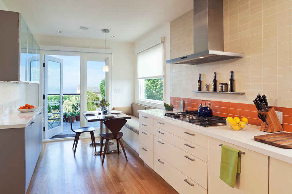 This is an example of a modern eat-in kitchen in San Francisco with flat-panel cabinets, beige cabinets and orange splashback.