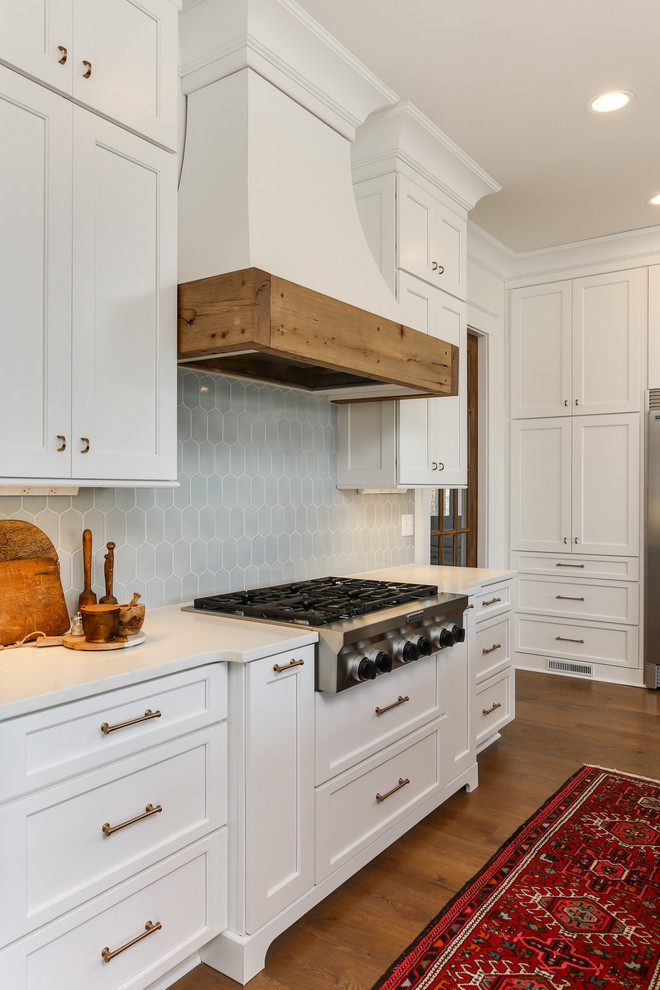 Large transitional l-shaped open plan kitchen in Raleigh with a farmhouse sink, recessed-panel cabinets, white cabinets, quartz benchtops, blue splashback, stainless steel appliances, medium hardwood floors, with island and white benchtop.