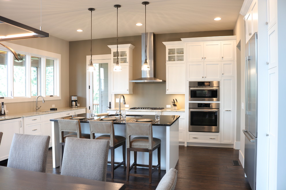Eat-in kitchen - mid-sized transitional l-shaped dark wood floor and brown floor eat-in kitchen idea in Charlotte with a single-bowl sink, shaker cabinets, white cabinets, granite countertops, beige backsplash, stone tile backsplash, stainless steel appliances, an island and brown countertops