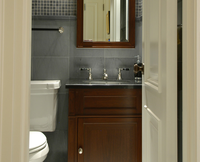 Small traditional powder room in New York with recessed-panel cabinets, dark wood cabinets, gray tile, stone tile, grey walls and an undermount sink.