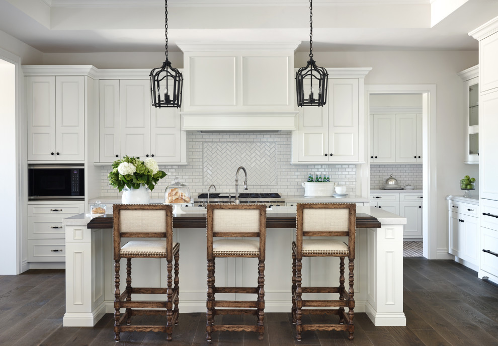 Design ideas for a traditional l-shaped kitchen in Phoenix with recessed-panel cabinets, white cabinets, white splashback, mosaic tile splashback, stainless steel appliances, dark hardwood floors, with island, brown floor and grey benchtop.