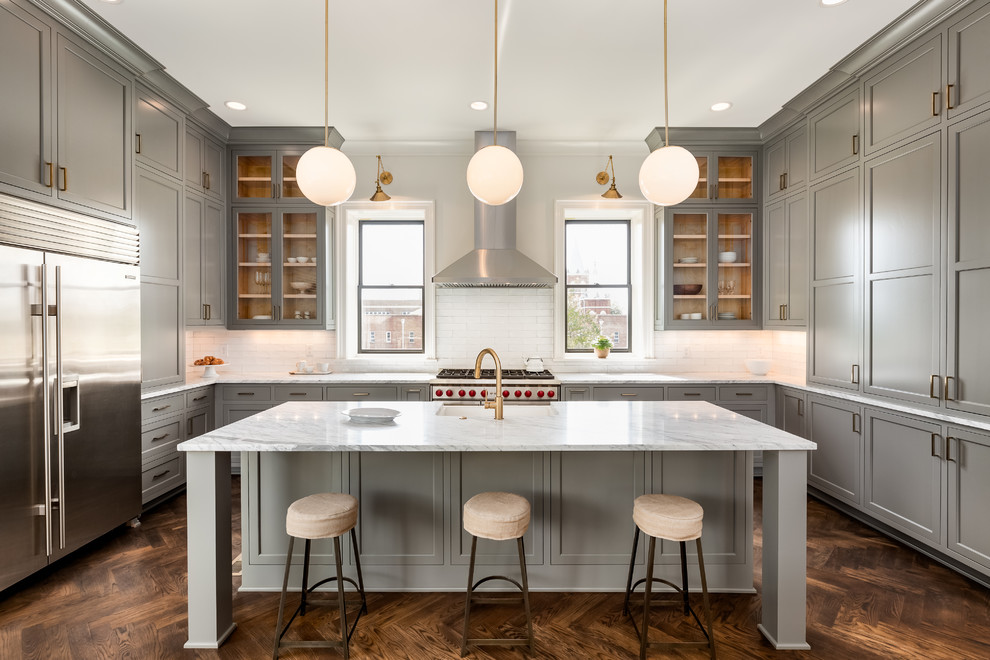 Design ideas for a transitional u-shaped kitchen in Nashville with grey cabinets, white splashback, stainless steel appliances, dark hardwood floors, with island, white benchtop and glass-front cabinets.