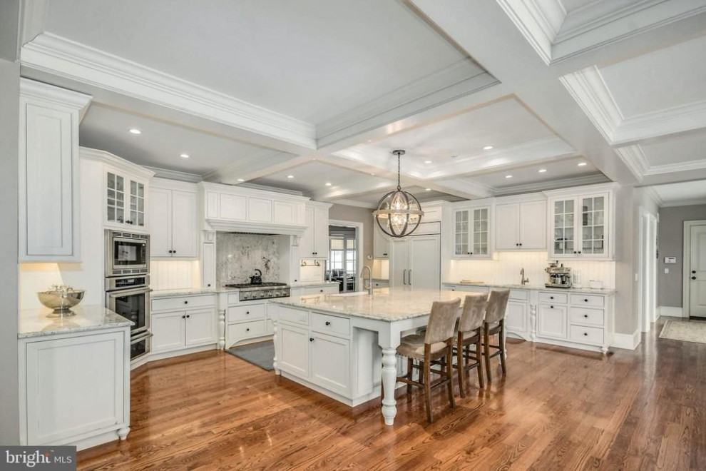 Design ideas for an expansive kitchen in Philadelphia with a belfast sink, beaded cabinets, white cabinets, wood splashback, medium hardwood flooring, an island and a coffered ceiling.
