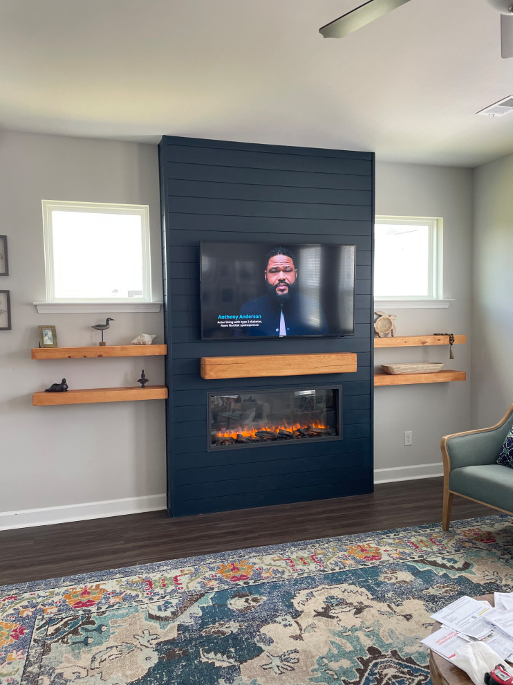 На фото: гостиная комната в морском стиле с синими стенами, стандартным камином, фасадом камина из вагонки, телевизором на стене, коричневым полом и стенами из вагонки