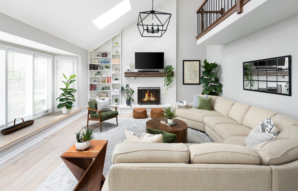 Mid-sized transitional open concept family room in Chicago with grey walls, light hardwood floors, a standard fireplace, a brick fireplace surround, a wall-mounted tv, brown floor and vaulted.