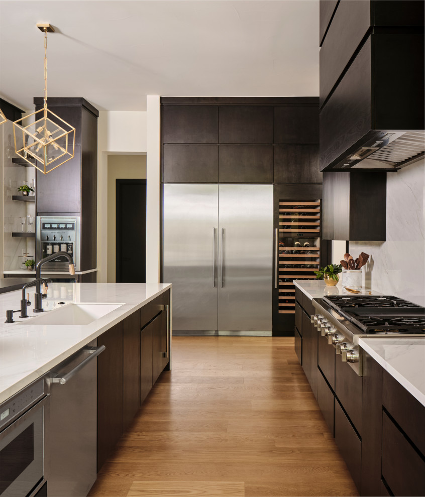 This is an example of a large contemporary l-shaped open plan kitchen in Denver with an undermount sink, flat-panel cabinets, dark wood cabinets, white splashback, stone slab splashback, stainless steel appliances, light hardwood floors, with island, beige floor, white benchtop and exposed beam.