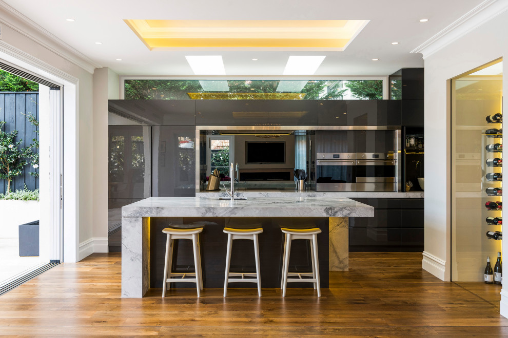 Photo of a modern l-shaped kitchen in Sydney with flat-panel cabinets, marble benchtops, grey splashback, limestone splashback, stainless steel appliances, medium hardwood floors and with island.