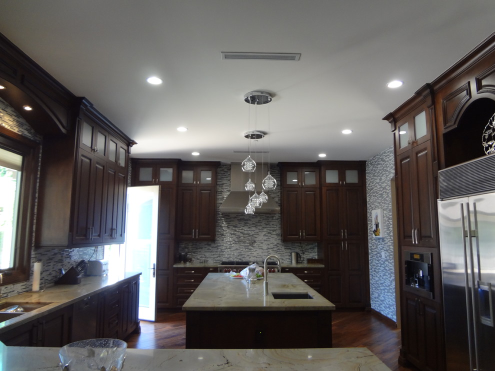 Photo of a traditional l-shaped eat-in kitchen in Los Angeles with raised-panel cabinets, dark wood cabinets, marble benchtops, white splashback, stone tile splashback and stainless steel appliances.
