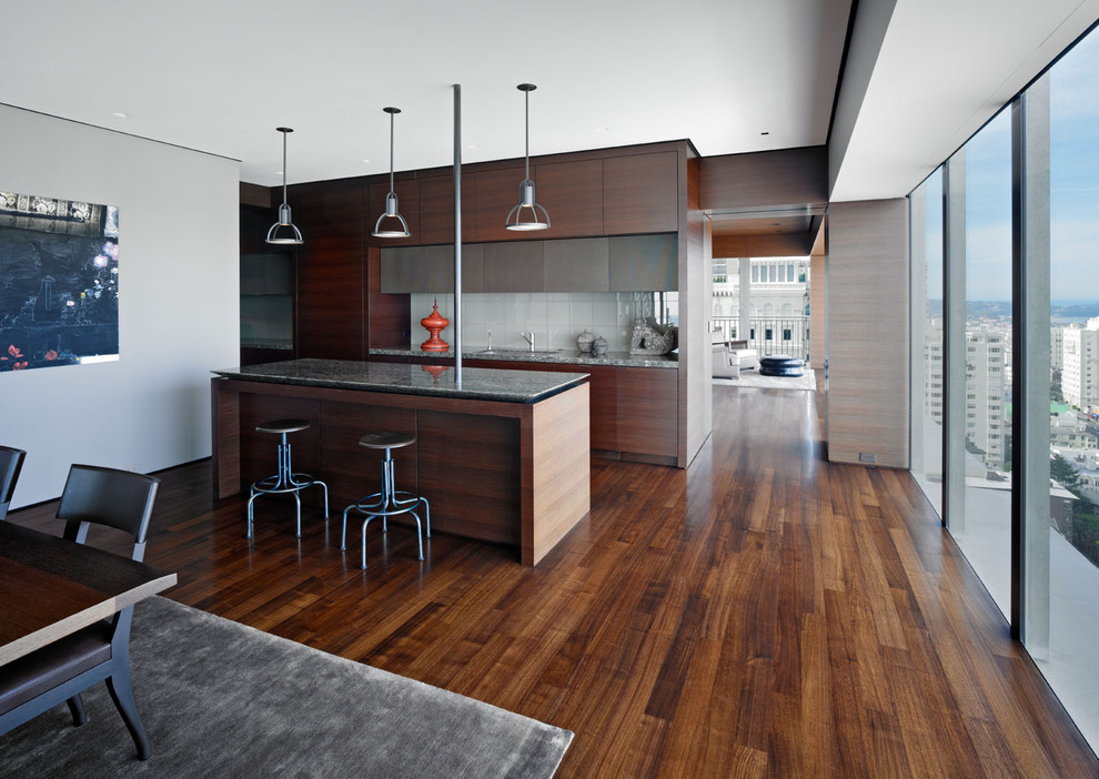 Photo of a modern eat-in kitchen in San Francisco with flat-panel cabinets, dark wood cabinets, white splashback, glass tile splashback and brown floor.