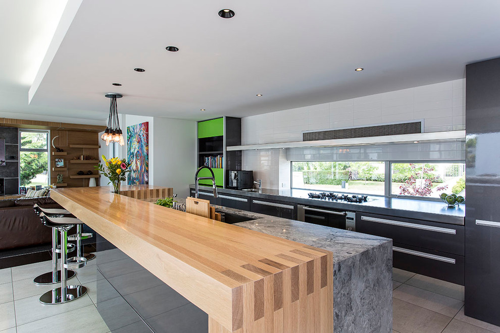 This is an example of a large contemporary galley eat-in kitchen in Christchurch with an undermount sink, flat-panel cabinets, black cabinets, wood benchtops, stainless steel appliances, ceramic floors, with island and grey floor.