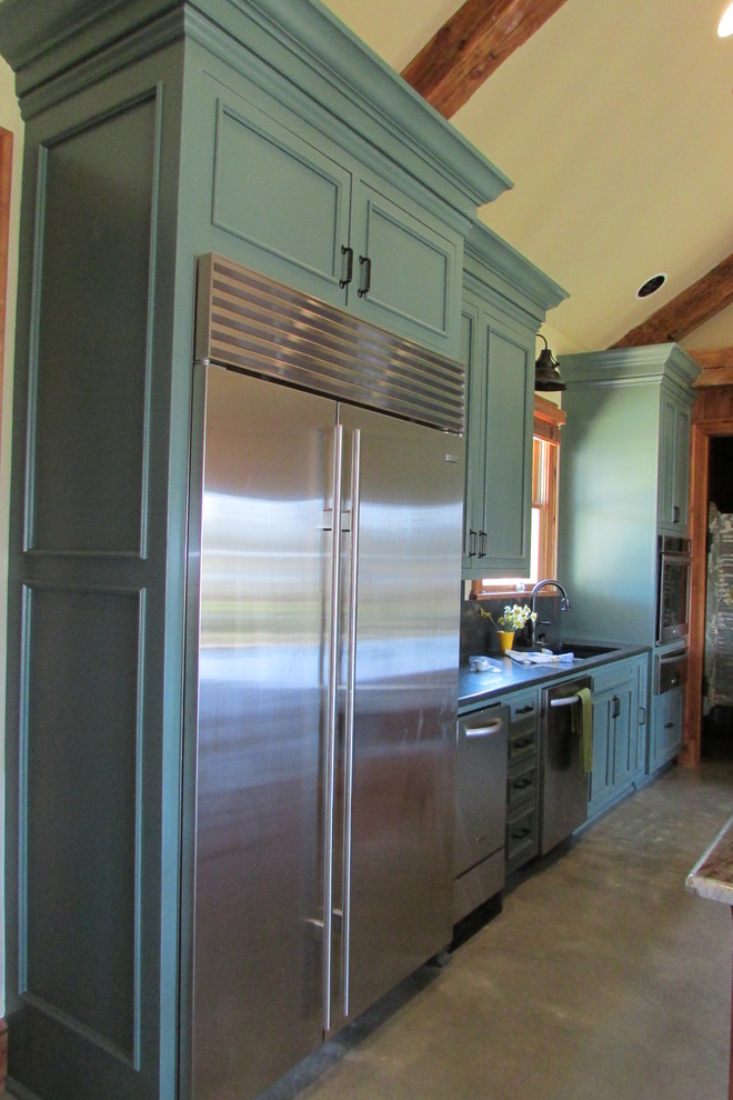 This is an example of a country open plan kitchen in New Orleans with beaded inset cabinets, granite benchtops, metallic splashback, stainless steel appliances and concrete floors.