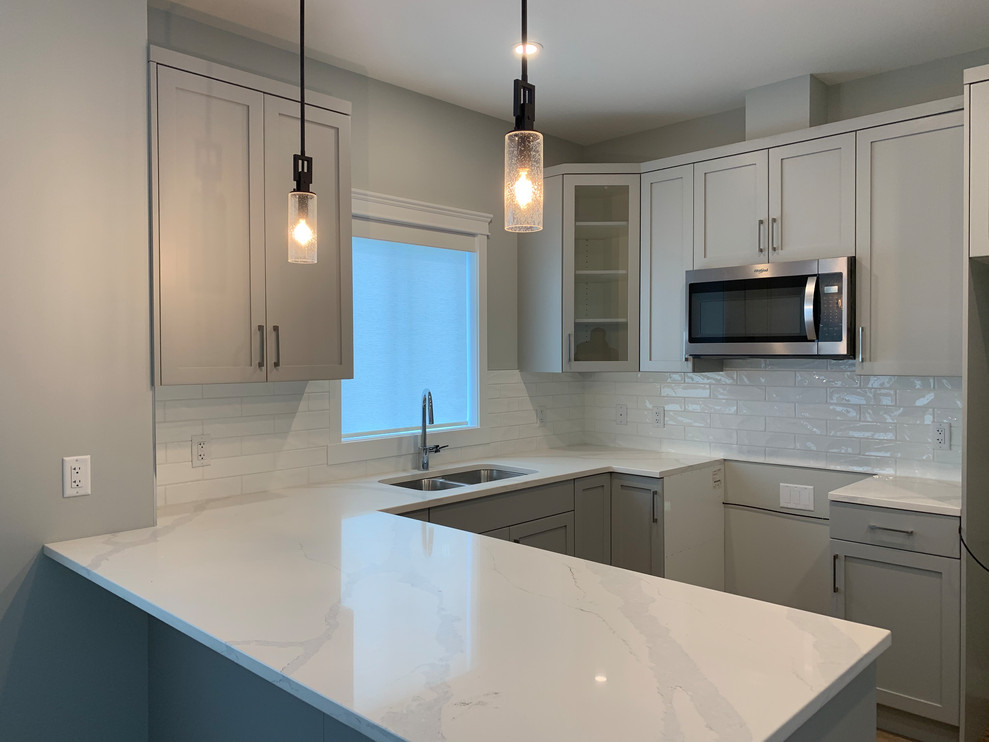 Small u-shaped vinyl floor and beige floor eat-in kitchen photo with a double-bowl sink, shaker cabinets, gray cabinets, white backsplash, ceramic backsplash, stainless steel appliances and an island