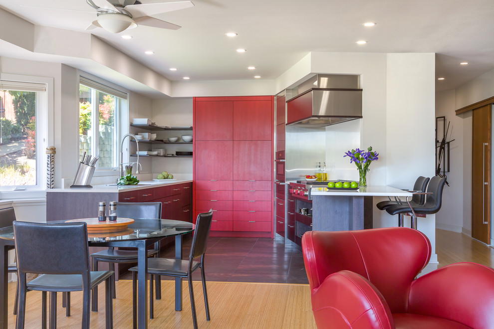 This is an example of a mid-sized contemporary u-shaped eat-in kitchen in Seattle with stainless steel appliances, red cabinets, an undermount sink, flat-panel cabinets, quartz benchtops, white splashback, stone slab splashback, porcelain floors and a peninsula.
