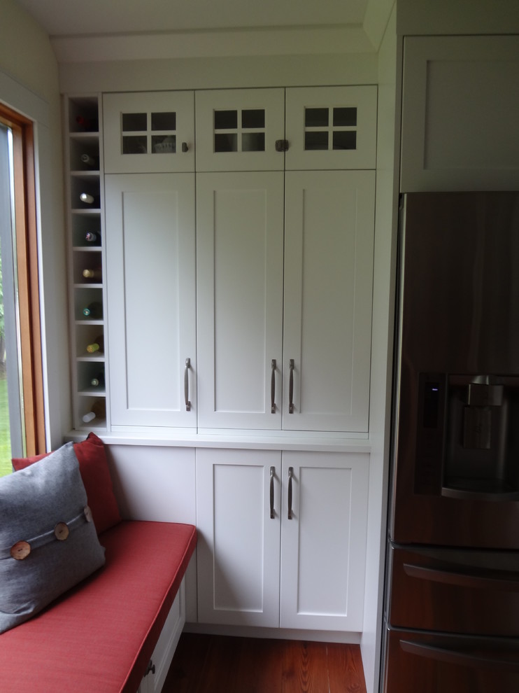 Example of a mid-sized transitional galley medium tone wood floor and brown floor kitchen design with an undermount sink, shaker cabinets, white cabinets, granite countertops, white backsplash, ceramic backsplash and stainless steel appliances