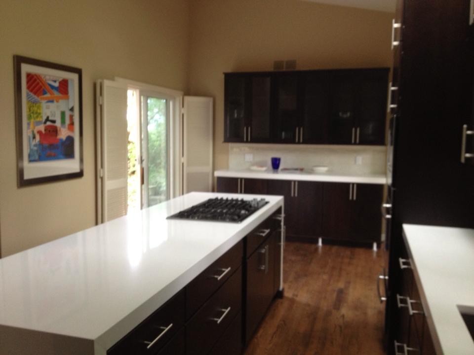 Kitchen - mid-sized transitional galley medium tone wood floor kitchen idea with an undermount sink, flat-panel cabinets, dark wood cabinets, quartz countertops, white backsplash, mosaic tile backsplash, stainless steel appliances and an island