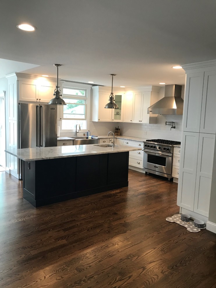 Example of a transitional u-shaped dark wood floor and brown floor kitchen design in New York with a farmhouse sink, recessed-panel cabinets, white cabinets, wood countertops, white backsplash, limestone backsplash, stainless steel appliances, an island and white countertops