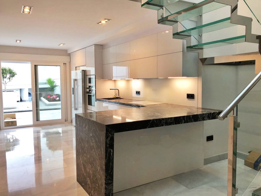 Photo of a modern l-shaped open plan kitchen in Other with an undermount sink, flat-panel cabinets, white cabinets, granite benchtops, white splashback, window splashback, white appliances, marble floors, a peninsula and white floor.
