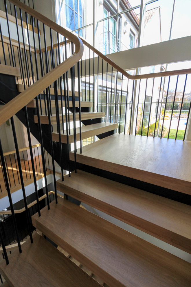 Photo of an expansive modern wood floating staircase in DC Metro with mixed railing and planked wall panelling.