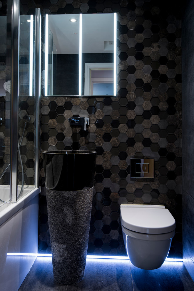Inspiration for a small contemporary kids bathroom in London with recessed-panel cabinets, black cabinets, a drop-in tub, a shower/bathtub combo, a wall-mount toilet, black tile, porcelain tile, black walls, porcelain floors and a vessel sink.