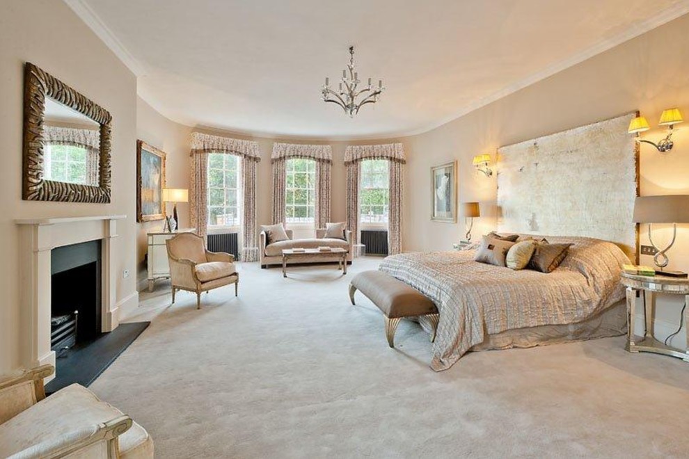 Expansive transitional master bedroom in London with beige walls, carpet, a standard fireplace, a metal fireplace surround and beige floor.