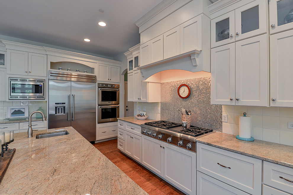 Photo of a transitional u-shaped eat-in kitchen in Chicago with a single-bowl sink, shaker cabinets, white cabinets, granite benchtops, metallic splashback, metal splashback, stainless steel appliances, medium hardwood floors and with island.