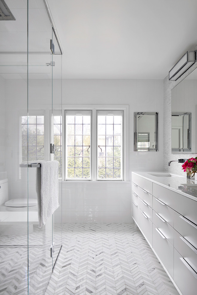 Walk-in shower - contemporary white tile and subway tile walk-in shower idea in New York with flat-panel cabinets, gray cabinets, an undermount sink, marble countertops and a one-piece toilet
