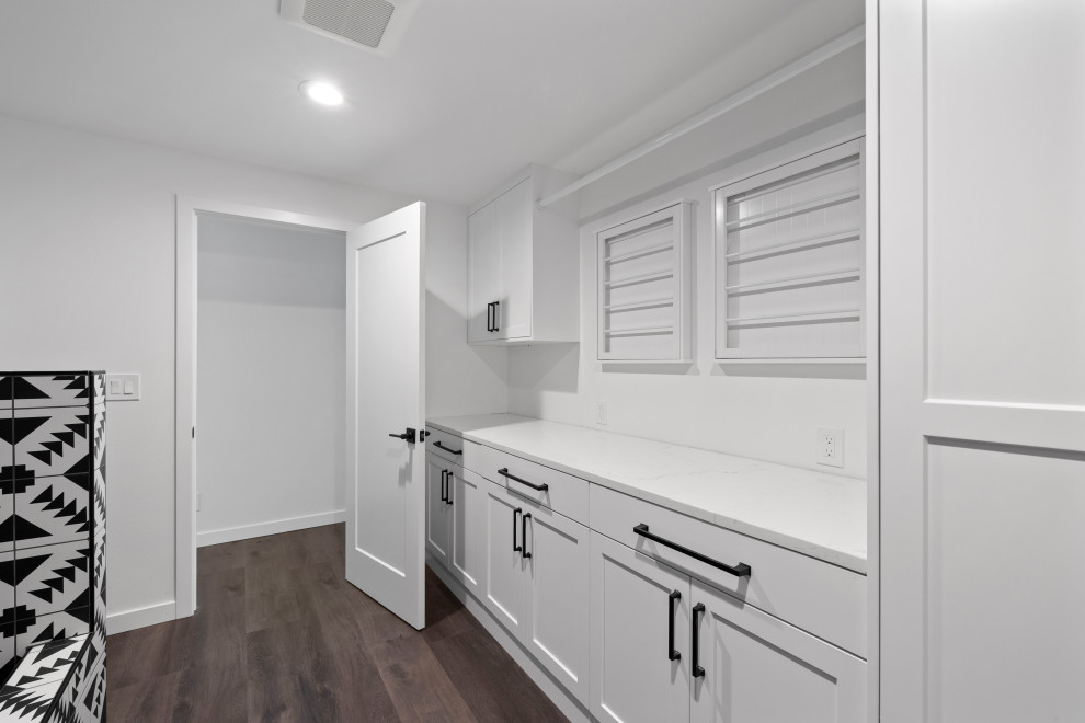 Example of a large transitional single-wall vinyl floor, brown floor and vaulted ceiling open concept kitchen design in Seattle with an undermount sink, shaker cabinets, white cabinets, quartz countertops, white backsplash, quartz backsplash, stainless steel appliances, an island and white countertops