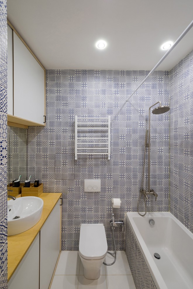 This is an example of a small contemporary master bathroom in Moscow with a shower/bathtub combo, blue tile, ceramic tile, porcelain floors, wood benchtops, flat-panel cabinets, white cabinets, an alcove tub, a vessel sink, a one-piece toilet, multi-coloured walls and a shower curtain.
