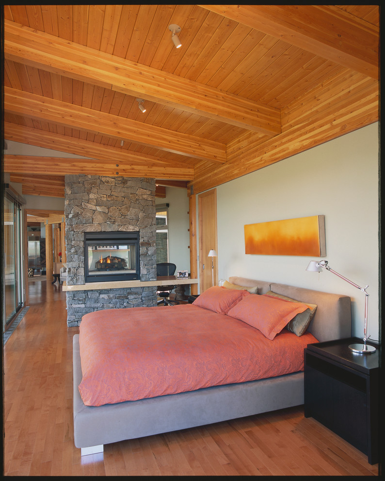 This is an example of a large contemporary master bedroom in Vancouver with white walls, light hardwood floors, a two-sided fireplace and a stone fireplace surround.