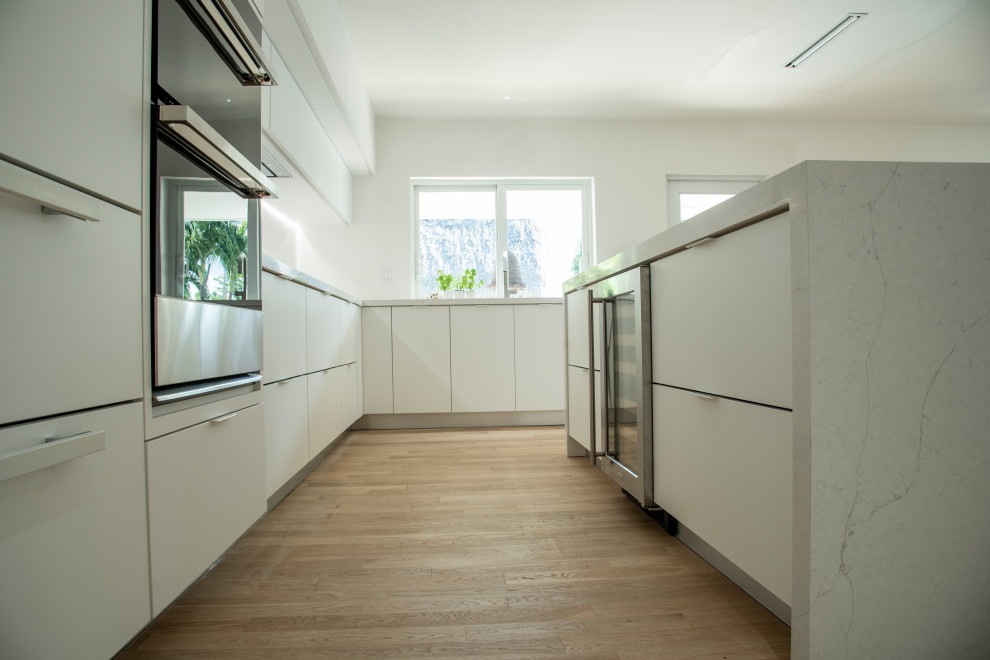 Large minimalist l-shaped medium tone wood floor and brown floor open concept kitchen photo in Miami with an undermount sink, flat-panel cabinets, white cabinets, quartz countertops, white backsplash, quartz backsplash, paneled appliances, an island and white countertops