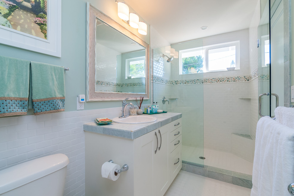 Photo of a mid-sized beach style master bathroom in Tampa with shaker cabinets, white cabinets, an open shower, a one-piece toilet, porcelain tile, green walls, ceramic floors, a drop-in sink, marble benchtops and white tile.